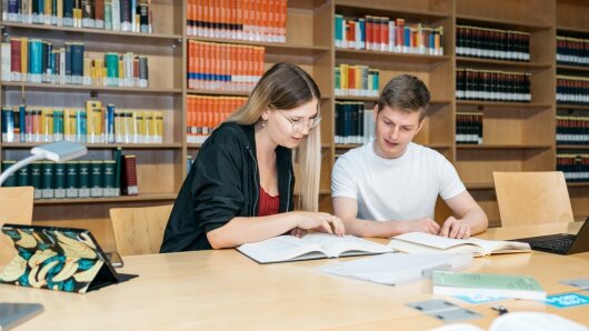 Zwei Studierende sitzen am Tisch und schauen gemeinsam in ein Buch.