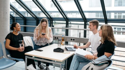 Studierende sitzen gemeinsam an einem Tisch und unterhalten sich.